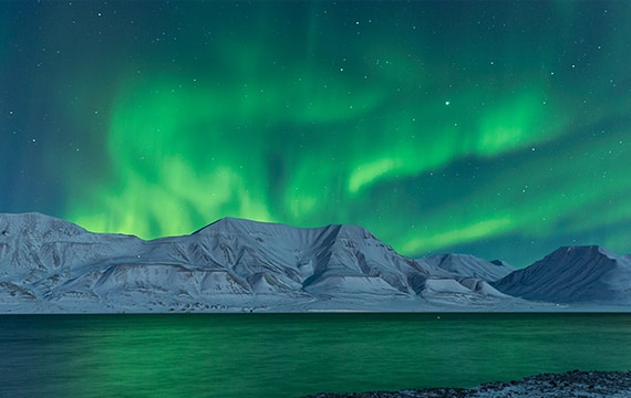 Im Postkartensatz Spitzbergen leuchtet ein Nordlicht vom Polarhimmel über dem Adventfjord.